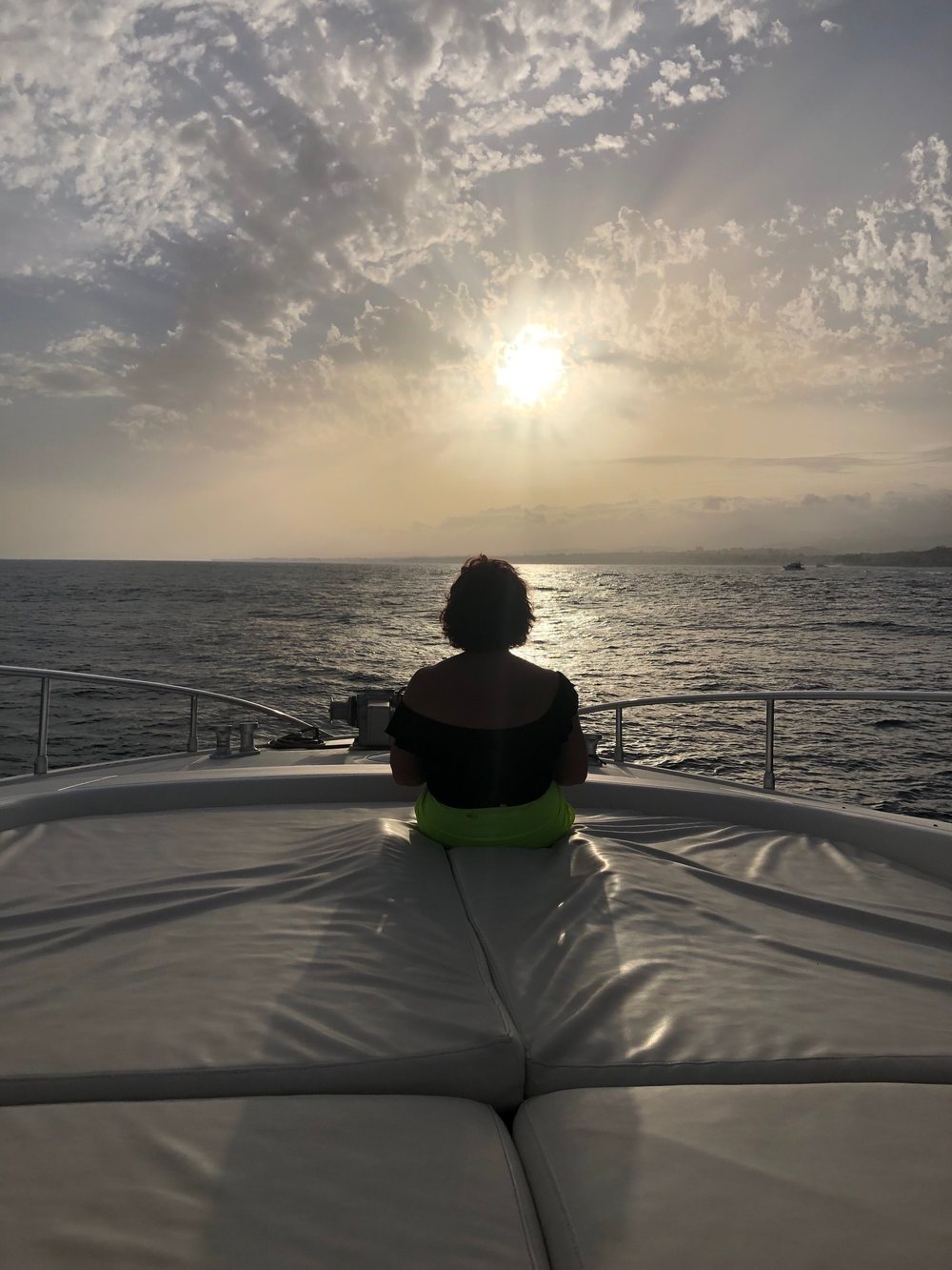 Susan East seated on the bow of a yacht at sunset, looking out over the sea